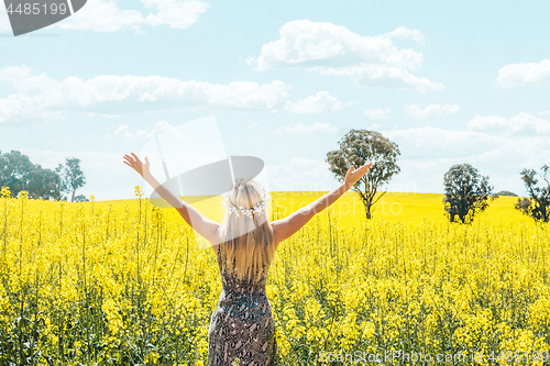 Image of Woman in dress arms in the air standing in front of olden canola fields
