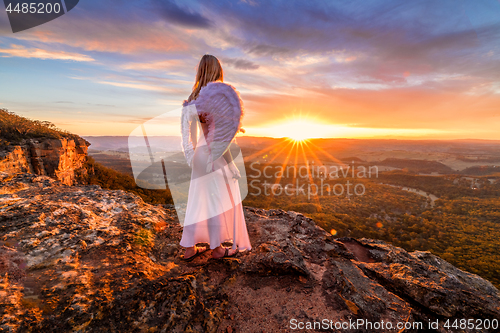 Image of Angelic woman with angel wings and white dress on mountain cliffs sunset