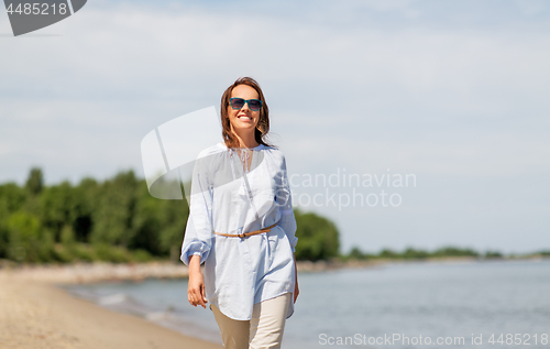 Image of happy smiling woman walking along summer beach