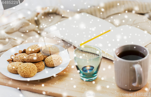 Image of cookies, tea and candle at home over snow