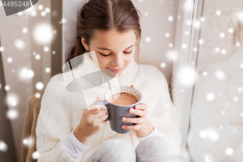 Image of girl in winter sweater with cacao mug at window