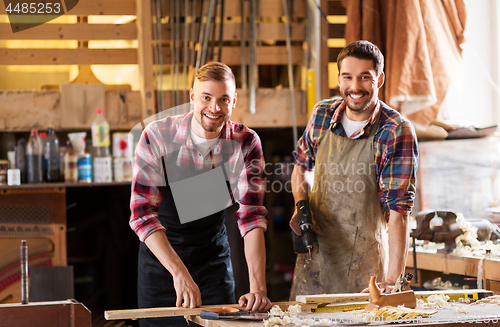 Image of happy carpenters with drill and board at workshop