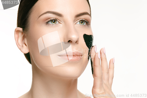 Image of Young beautiful woman applying a mask for the face of the therapeutic black mud. Spa treatment