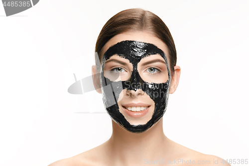 Image of Young beautiful woman applying a mask for the face of the therapeutic black mud. Spa treatment