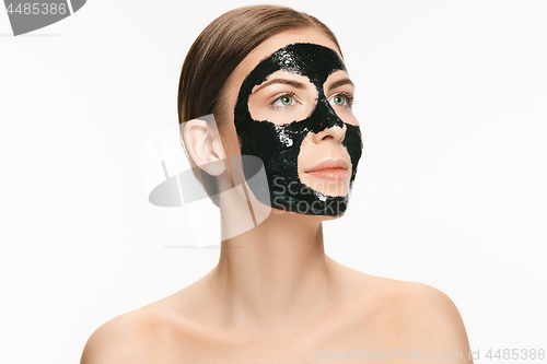 Image of Young beautiful woman applying a mask for the face of the therapeutic black mud. Spa treatment