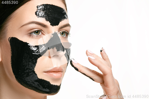 Image of Young beautiful woman applying a mask for the face of the therapeutic black mud. Spa treatment