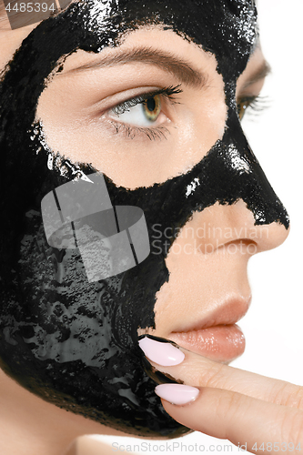 Image of Young beautiful woman applying a mask for the face of the therapeutic black mud. Spa treatment