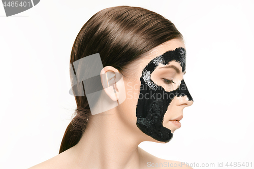 Image of Young beautiful woman applying a mask for the face of the therapeutic black mud. Spa treatment