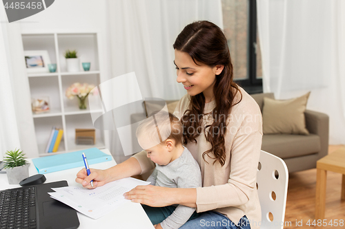 Image of happy mother with baby and papers working at home