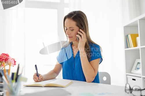 Image of woman with notepad calling on smartphone at office