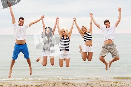 Image of friends in striped clothes running along beach