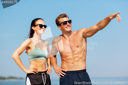 Image of happy couple in sports clothes and shades on beach