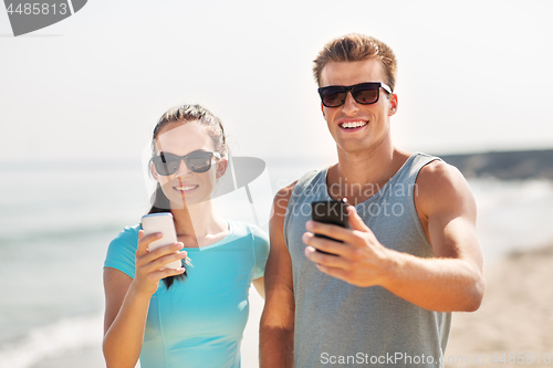 Image of couple in sports clothes with smartphones on beach