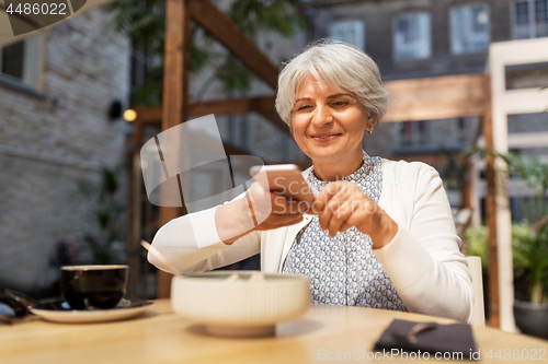 Image of senior woman photographing food at street cafe