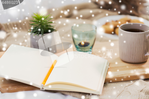 Image of diary, tea and candle in holder at home over snow