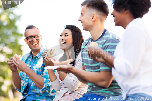 Image of happy friends eating sandwiches and pizza outdoors