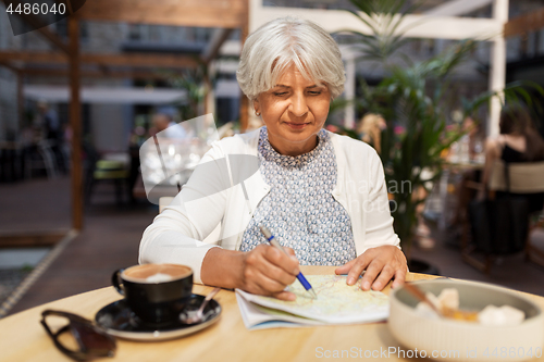 Image of senior woman with map and coffee at street cafe