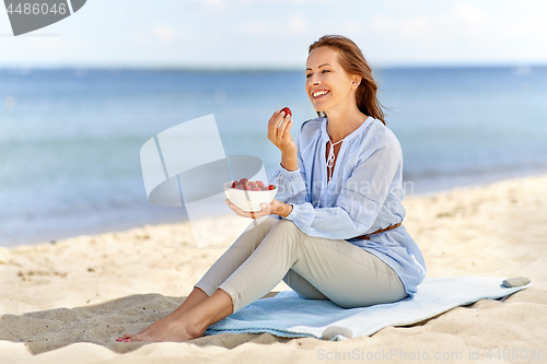 Image of happy woman eating strawberries on summer beach