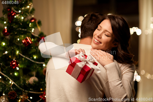 Image of happy couple with christmas gift hugging at home