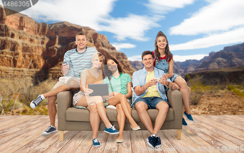 Image of friends with tablet pc and smartphones sit on sofa