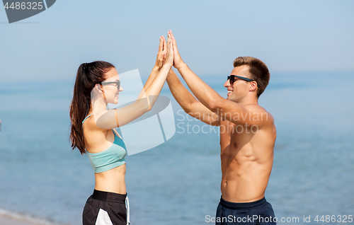 Image of happy couple in sports clothes and shades on beach