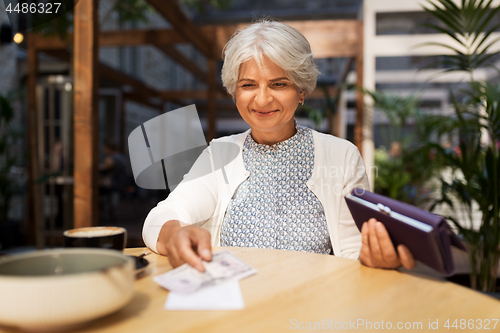 Image of senior woman with money paying bill at cafe