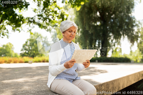 Image of senior woman reading newspaper at summer park