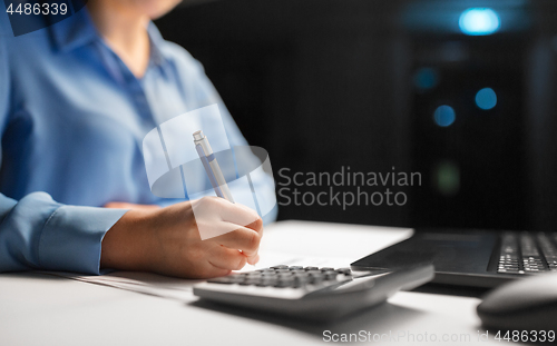 Image of woman with calculator and papers at night office