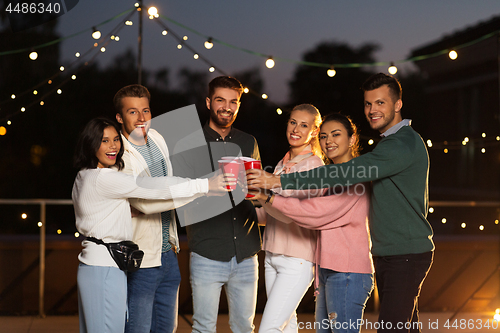 Image of friends clinking party cups on rooftop at night