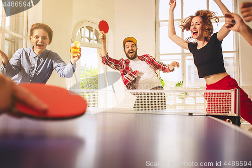 Image of Group of happy young friends playing ping pong table tennis