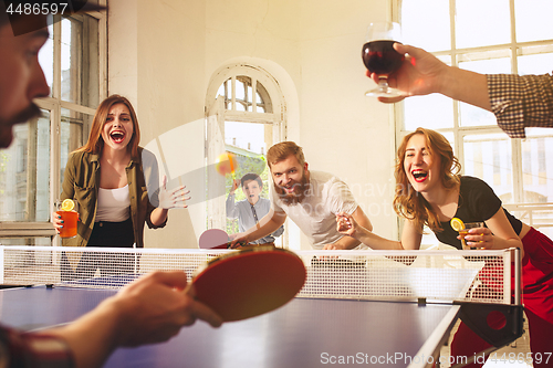 Image of Group of happy young friends playing ping pong table tennis