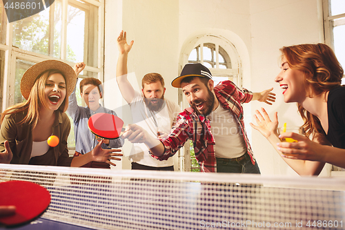 Image of Group of happy young friends playing ping pong table tennis