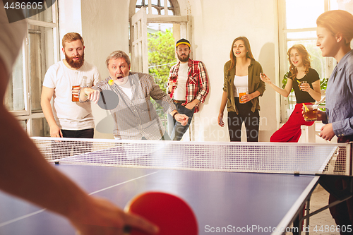 Image of Group of happy young friends playing ping pong table tennis