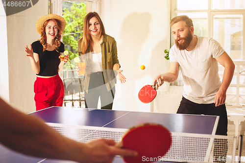 Image of Group of happy young friends playing ping pong table tennis