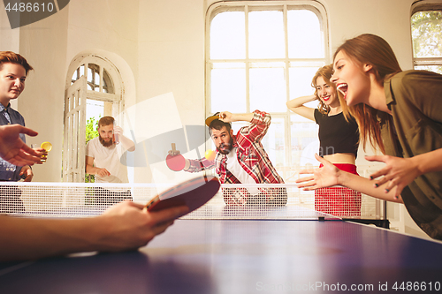 Image of Group of happy young friends playing ping pong table tennis