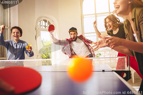 Image of Group of happy young friends playing ping pong table tennis