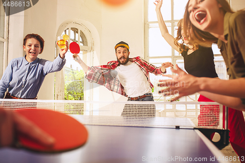 Image of Group of happy young friends playing ping pong table tennis