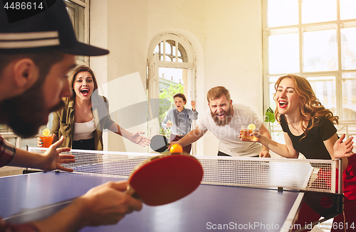 Image of Group of happy young friends playing ping pong table tennis