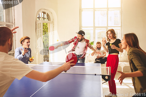 Image of Group of happy young friends playing ping pong table tennis