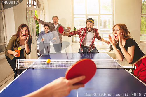 Image of Group of happy young friends playing ping pong table tennis