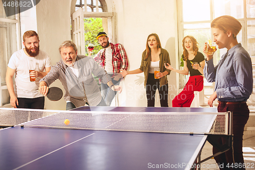 Image of Group of happy young friends playing ping pong table tennis