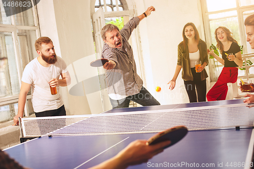 Image of Group of happy young friends playing ping pong table tennis