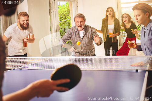 Image of Group of happy young friends playing ping pong table tennis