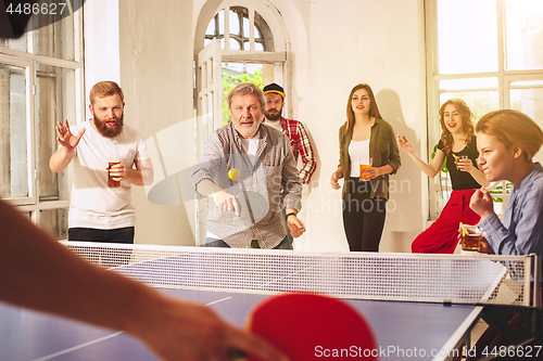 Image of Group of happy young friends playing ping pong table tennis