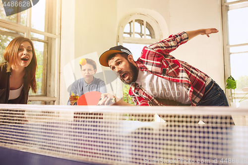 Image of Group of happy young friends playing ping pong table tennis