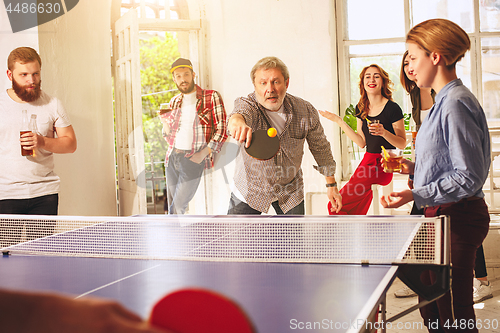 Image of Group of happy young friends playing ping pong table tennis