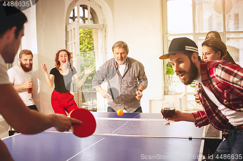 Image of Group of happy young friends playing ping pong table tennis