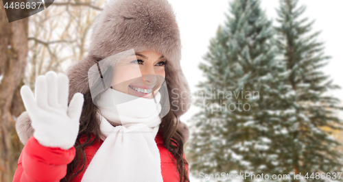 Image of happy woman in hat waving hand over winter forest