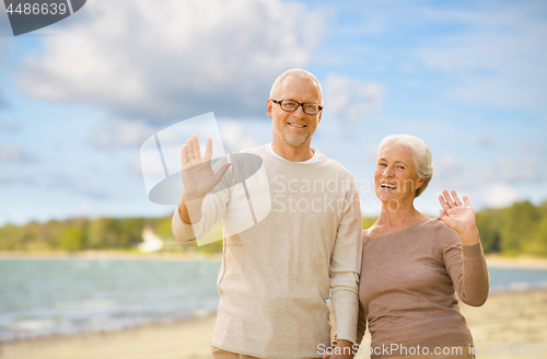 Image of happy senior couple waving hands on beach