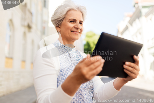 Image of smiling senior woman with tablet pc on city street
